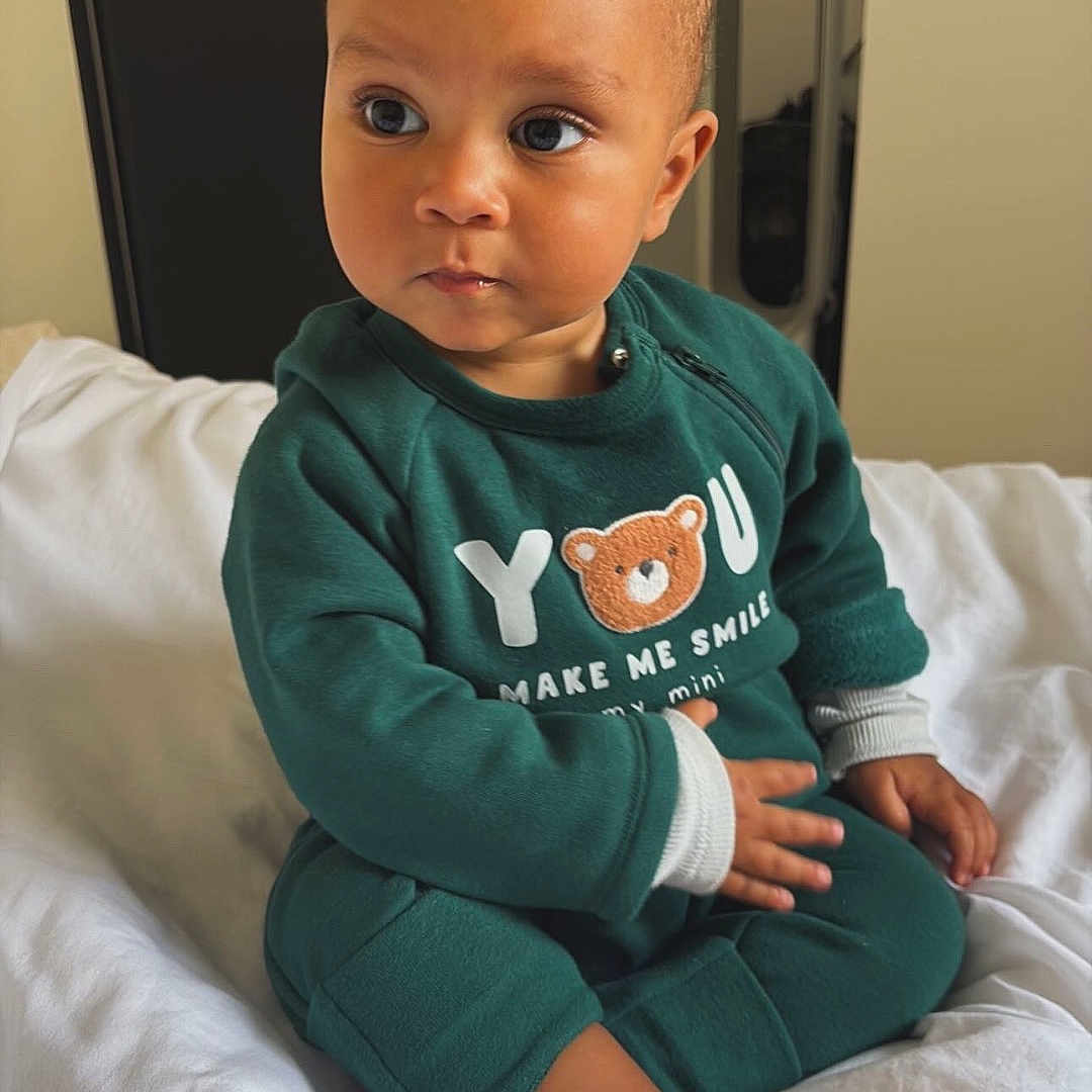 Simao participe au concours pour gagner de l'argent avec cette photo : baby, bear_design, bed, casual, child, cozy, curious, cute, door, expression, face, feet, green_clothing, hand, indoors, mirror, portrait, room, sitting, white_bed