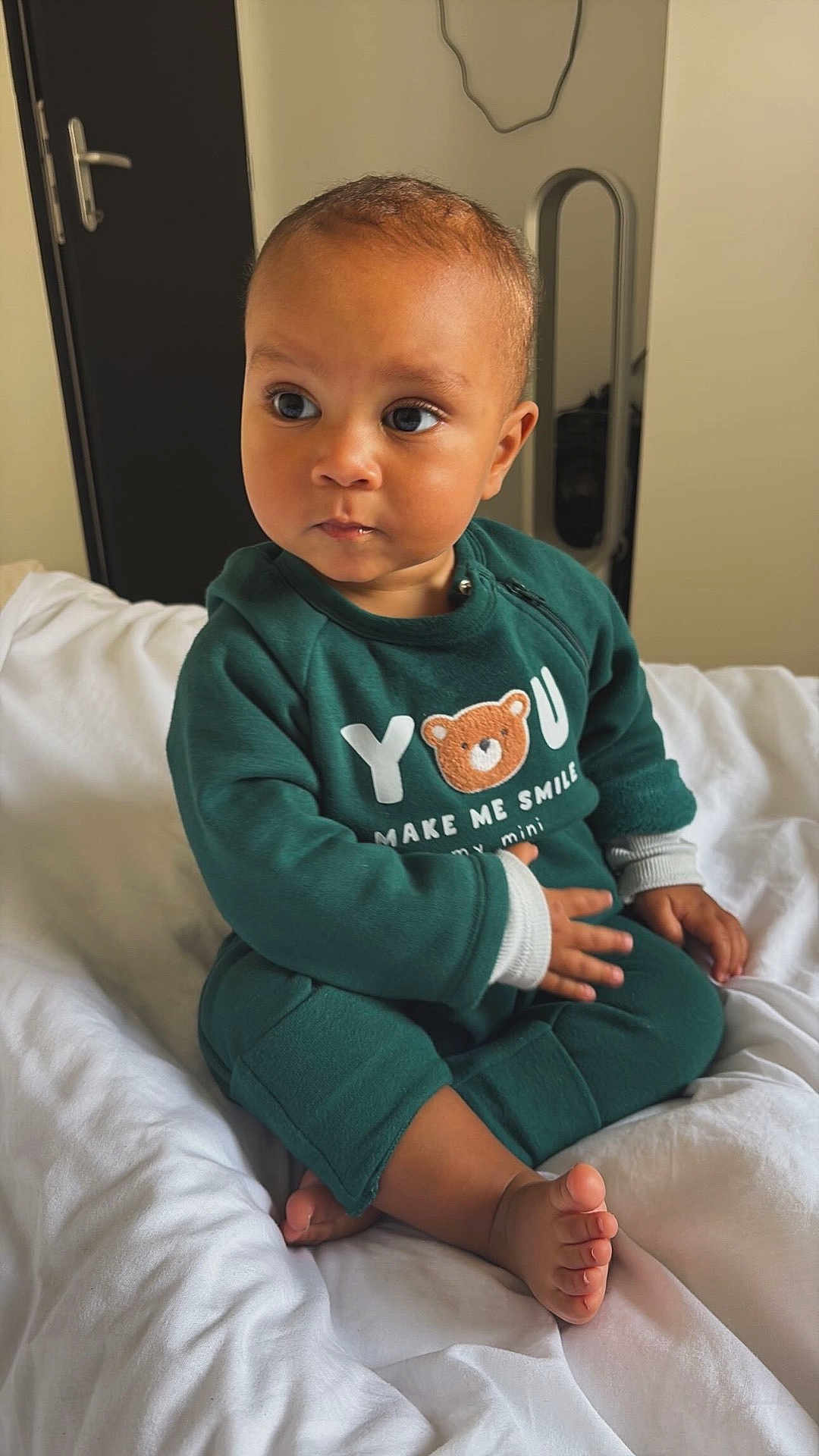 Simao participe au concours pour gagner de l'argent avec cette photo : baby, bear_design, bed, casual, child, cozy, curious, cute, door, expression, face, feet, green_clothing, hand, indoors, mirror, portrait, room, sitting, white_bed