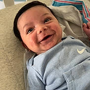 Carter is registered to the contest to win money with this photo: baby, blanket, blue_clothing, closeup, crib, cute, expression, face, happy, head, indoors, infant, light, lying_down, newborn, person, skin, smile, soft_fabric, young_child