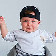 Mattias joined the competition — help win amazing prizes! baby, child, cap, smile, blue_eyes, teddy_bear_patch, light_shirt, sitting, raised_arms, happy, studio, minimalist_background, cute, portrait, infant, hands_up, casual_clothing, headwear, expression, indoor