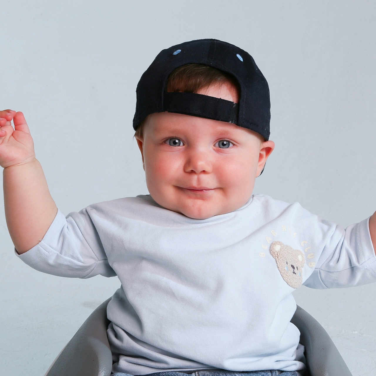 Mattias joined the competition — help win amazing prizes! baby, blue_eyes, cap, casual_clothing, child, cute, expression, hands_up, happy, headwear, indoor, infant, light_shirt, minimalist_background, portrait, raised_arms, sitting, smile, studio, teddy_bear_patch
