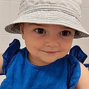Margot participe au concours pour gagner de l'argent avec cette photo : toddler, child, hat, bucket_hat, blue_dress, smile, face, person, indoor, cute, fashion, portrait, young_child, clothing, headwear, eyes, skin, shopping_cart, background, tile_wall