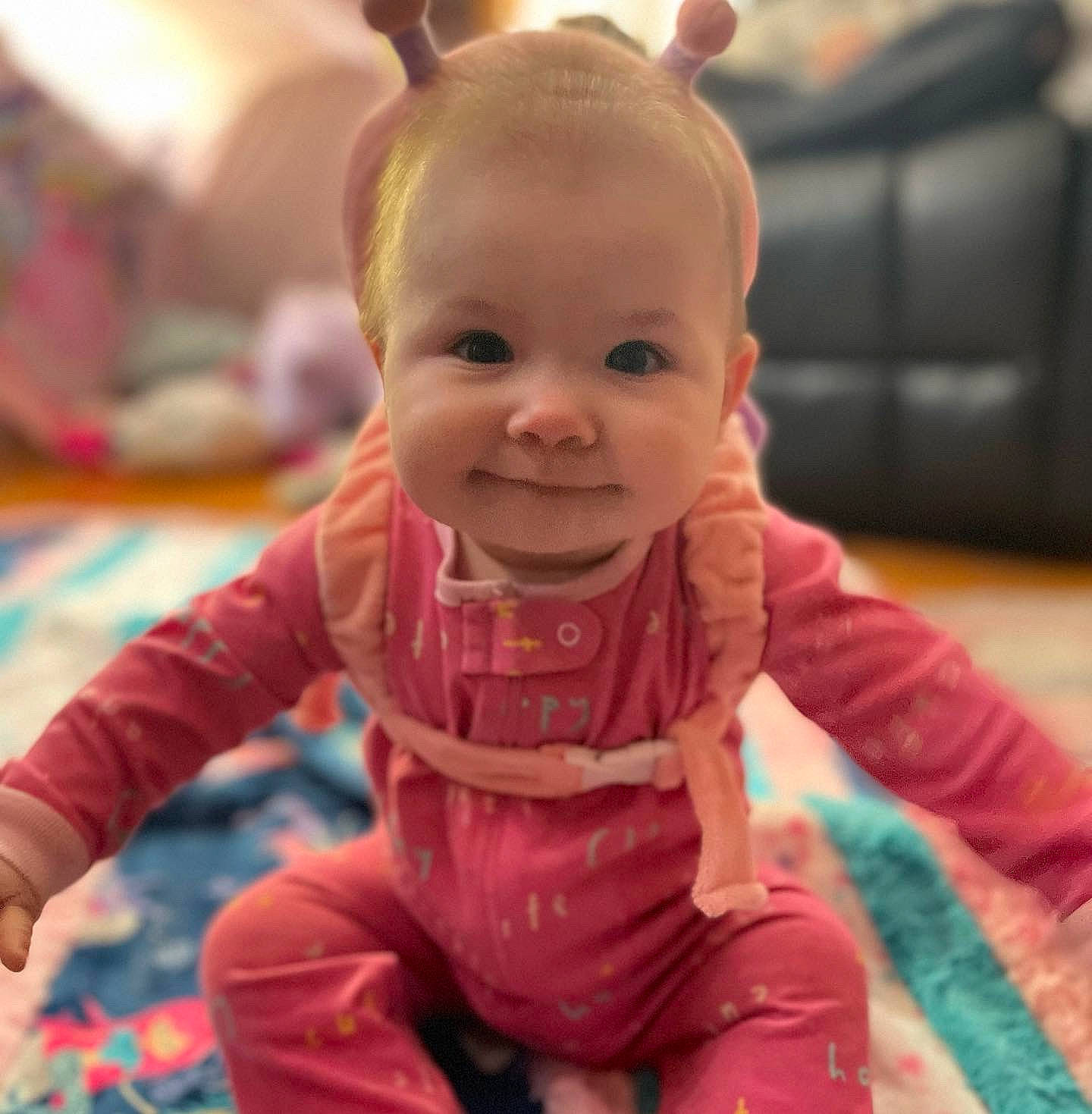 Aspen is registered to the contest to win money with this photo: baby, baby_toddler_clothing, cheek, child, chin, eye, fictional_character, finger, flooring, fun, happy, human_body, joy, magenta, person, pink, room, sitting, skin, smile