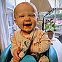 baby, smiling, high_chair, bib, indoor, child, face, happy, infant, window, lamp, plant, potted_plant, furniture, clothing, person, seat, home, cute, expression