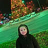 child, smiling, coat, hood, christmas_tree, night, lights, outdoor, grass, holiday, festive, decoration, streetlight, happy, person, winter, tree, park, celebration, season
