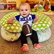 Bentley is registered to the contest to win money with this photo: baby, child, football, sports, bills, cushion, polka_dot, green, blue, white, carpet, indoor, smiling, sitting, toys, playroom, cute, feet, clothing, person