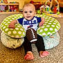 baby, child, football, sports, bills, cushion, polka_dot, green, blue, white, carpet, indoor, smiling, sitting, toys, playroom, cute, feet, clothing, person