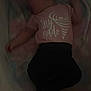 Oaklynn is registered to the contest to win money with this photo: baby, infant, newborn, sleeping, crib, onesie, blanket, shirt, text_on_shirt, ear, arm, hand, legs, pants, low_light, night, mattress, safety_label, portrait, indoors