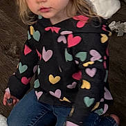 Alivia is registered to the contest to win money with this photo: child, toddler, girl, heart_pattern, hoodie, jeans, sitting, kneeling, blue_eyes, blond_hair, earring, pillow, blanket, wood_floor, indoor, candid_photo, toy_in_hand, portrait, cozy, neutral_expression