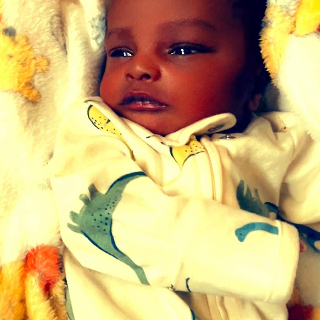 Kenyadi is registered to the contest to win money with this photo: baby, infant, blanket, pajamas, dinosaur_print, sleepwear, child, cute, soft_texture, warm, resting, indoors, portrait, newborn, face, cozy, young_child, lying_down, comfort, adorable