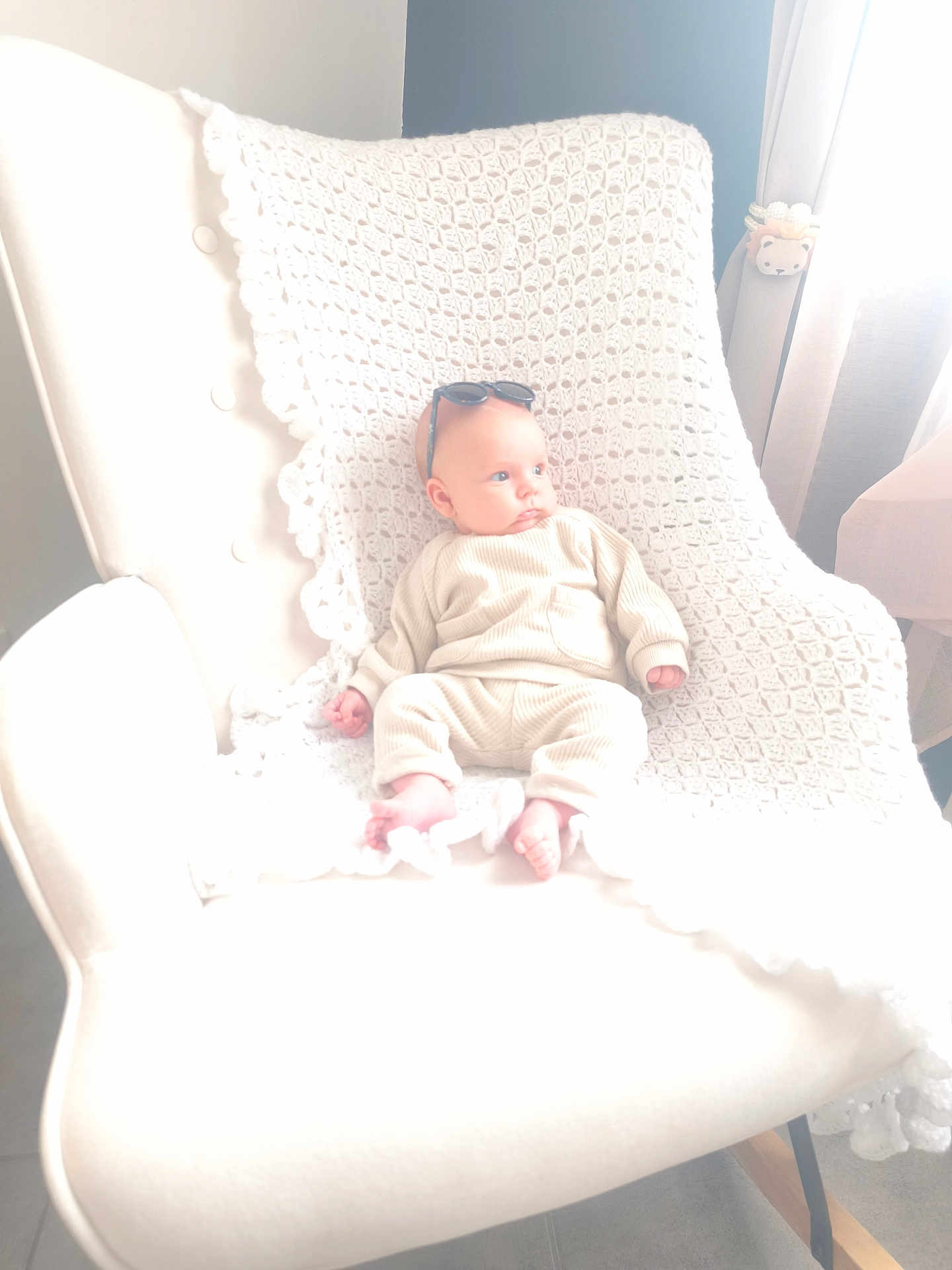 élyo a rejoint le concours — aidez-le/la à gagner de superbes lots ! baby, child, infant, chair, blanket, crochet, knitwear, sunglasses, indoor, window, curtain, floor, modern_furniture, soft_lighting, person, footwearless, relaxing, cozy, neutral_colors, portrait