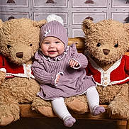 Ivy is registered to the contest to win money with this photo: baby, bench, child, cozy, cute, decor, happy, hat, indoor, knitted_clothing, plush, pom_pom, portrait, purple_dress, smiling, stuffed_animal, teddy_bear, toy, warm_clothing, wooden_furniture