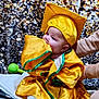 baby, child, graduation_gown, graduation_cap, yellow_clothing, blanket, indoor, person, cute, chewing, sitting, soft_toy, supporting_hand, floor, celebration, portrait, infant, colorful_background, fabric, smiling