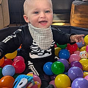 Jordi joined the competition — help win amazing prizes! baby, child, ball_pit, colorful_balls, toys, skeleton_outfit, smiling, indoor, window, daylight, happy, playtime, infant, clothing, bib, face, person, home, furniture, cushion