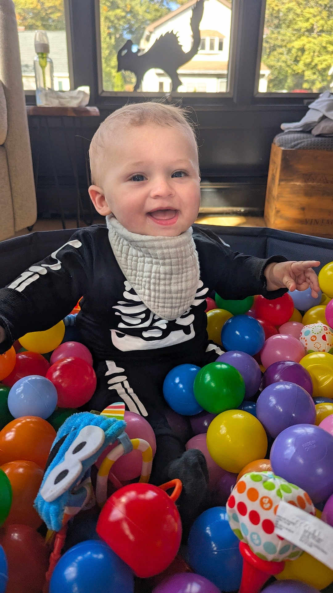 Jordi joined the competition — help win amazing prizes! baby, child, ball_pit, colorful_balls, toys, skeleton_outfit, smiling, indoor, window, daylight, happy, playtime, infant, clothing, bib, face, person, home, furniture, cushion