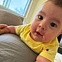 Jeremy is registered to the contest to win money with this photo: baby, infant, child, face, eyes, cheeks, yellow_shirt, champion_logo, hand, arm, pillow, bed, window, indoors, portrait, close_up, curious, smile, skin, hair