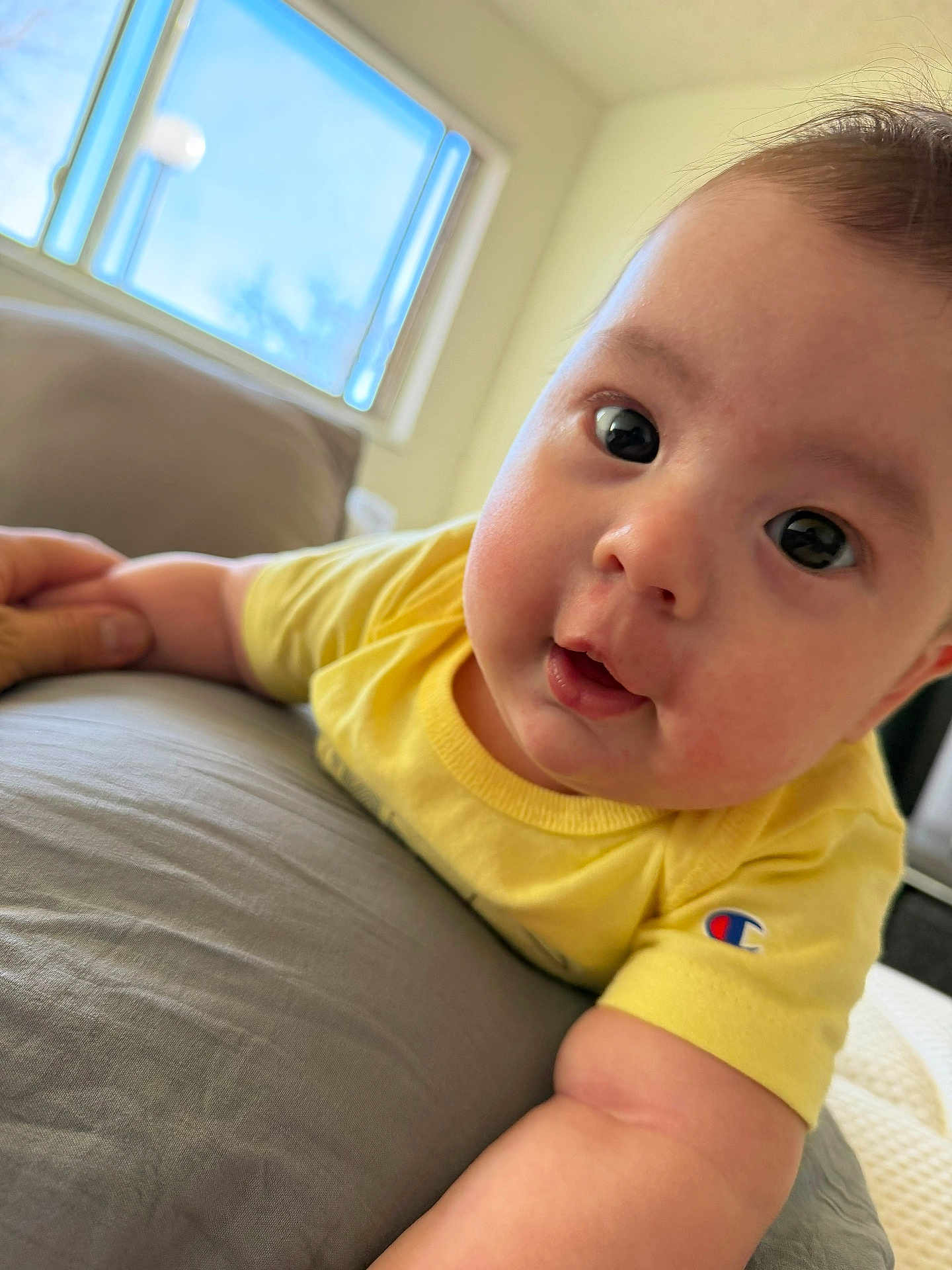 Jeremy is registered to the contest to win money with this photo: baby, infant, child, face, eyes, cheeks, yellow_shirt, champion_logo, hand, arm, pillow, bed, window, indoors, portrait, close_up, curious, smile, skin, hair