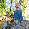 adventure, blue_shirt, boy, casual_clothing, child, creek, daytime, forest, happy, nature, outdoor, pants, play, rocks, shoes, smiling, stick, sunlight, trees, water