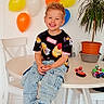 balloons, boy, carpet, casual_clothing, chair, child, colorful, furniture, happy, home, indoor, jeans, plant, playful, portrait, potted_plant, smiling, table, toys, tshirt