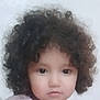 baby_face, casual_clothing, child, close_up, curly_hair, cute, expression, face, head_and_shoulders, indoor, innocent, looking_at_camera, natural_light, neutral_background, person, portrait, real_photo, soft_focus, soft_lighting, young