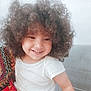 candid, casual, child, colorful, curly_hair, cute, face, hair, happy, indoor, joyful, patterned_fabric, person, portrait, sitting, skin, smiling, toddler, white_shirt, young_child