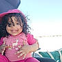 bright_sky, casual_wear, cheerful, child, curly_hair, cute, fun, hand_gesture, happy, hat, outdoor, person, pink_clothing, playful, portrait, sitting, smile, sunlight, toddler, young