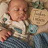 baby, sleeping, blanket, pacifier, wooden_plaque, infant, cozy, cute, newborn, child, face, hand, soft, bed, clothing, blue_blanket, resting, indoor, portrait, peaceful