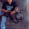 person, dog, french_bulldog, glasses, tshirt, nirvana, jeans, butterfly, chair, furniture, indoor, relaxed, pet, casual, sitting, black_dog, ripped_jeans, wood_floor, home, comfort