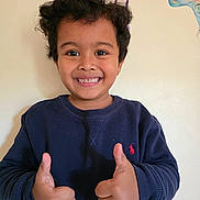 Shritik joined the competition — help win amazing prizes! child, smiling, thumbs_up, curly_hair, navy_sweatshirt, indoor, wall_art, butterflies, happy, person, portrait, casual_clothing, positive_gesture, young, cute, face, head, expression, light_background, earring