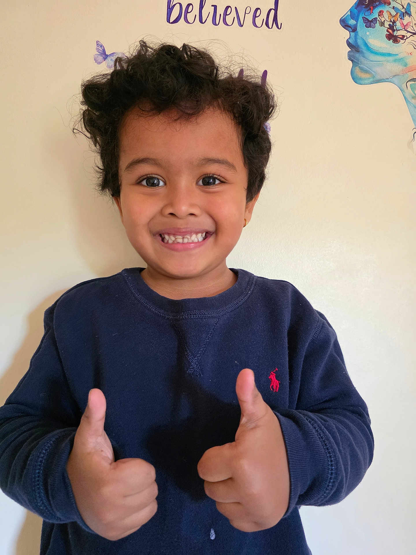 Shritik joined the competition — help win amazing prizes! child, smiling, thumbs_up, curly_hair, navy_sweatshirt, indoor, wall_art, butterflies, happy, person, portrait, casual_clothing, positive_gesture, young, cute, face, head, expression, light_background, earring