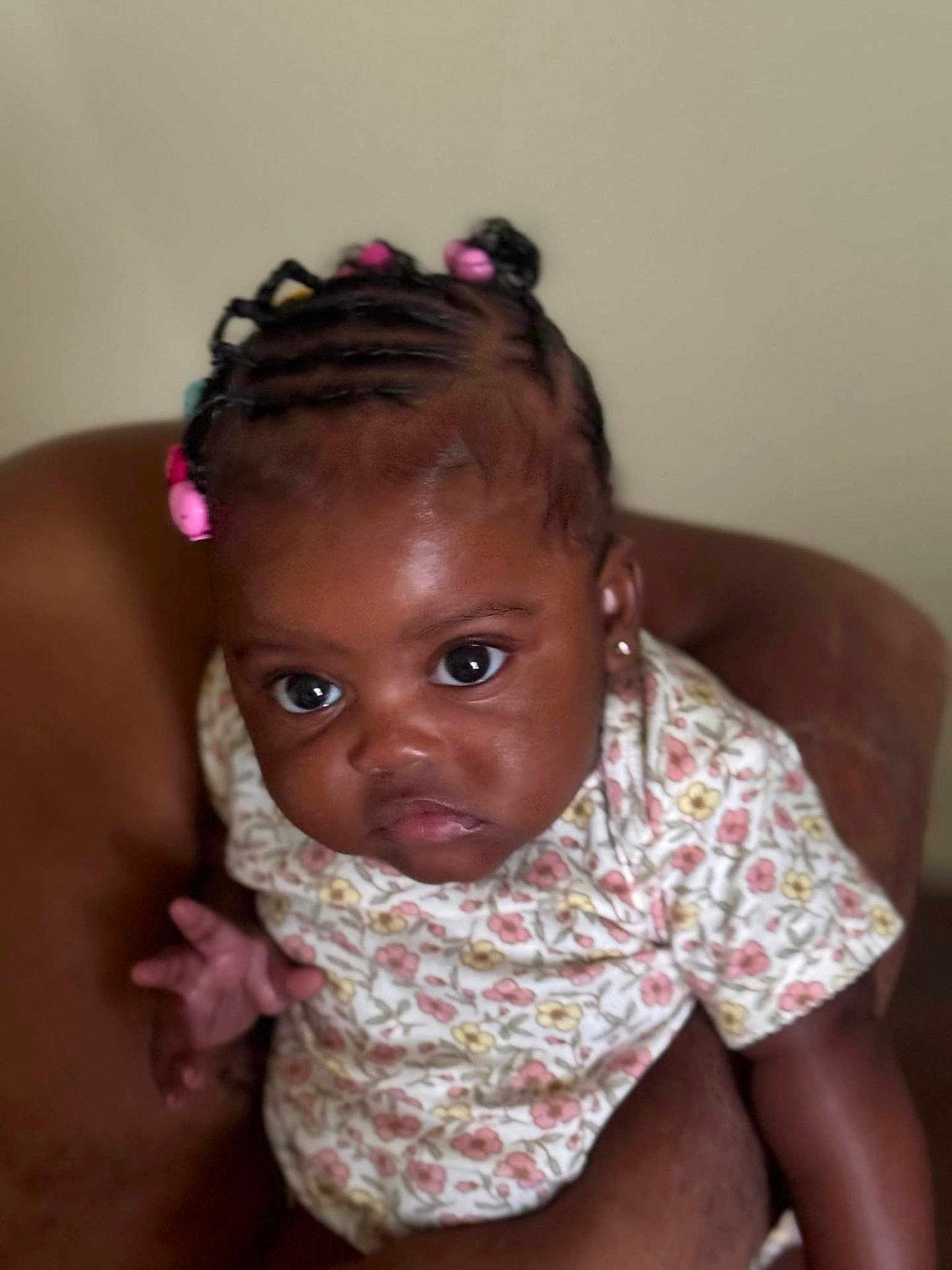 Sariah is registered to the contest to win money with this photo: baby, child, braided_hair, beads, floral_outfit, cute, closeup, expression, face, hand, adult_hand, indoor, portrait, person, skin, head, sitting, holding, infant, young_child
