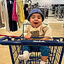 apparel, baby, bear_sweater, blue_hat, child, clothes, clothing_store, cute, flooring, happy, indoor, infant, person, racks, retail, shopping, shopping_cart, smiling, socks, store
