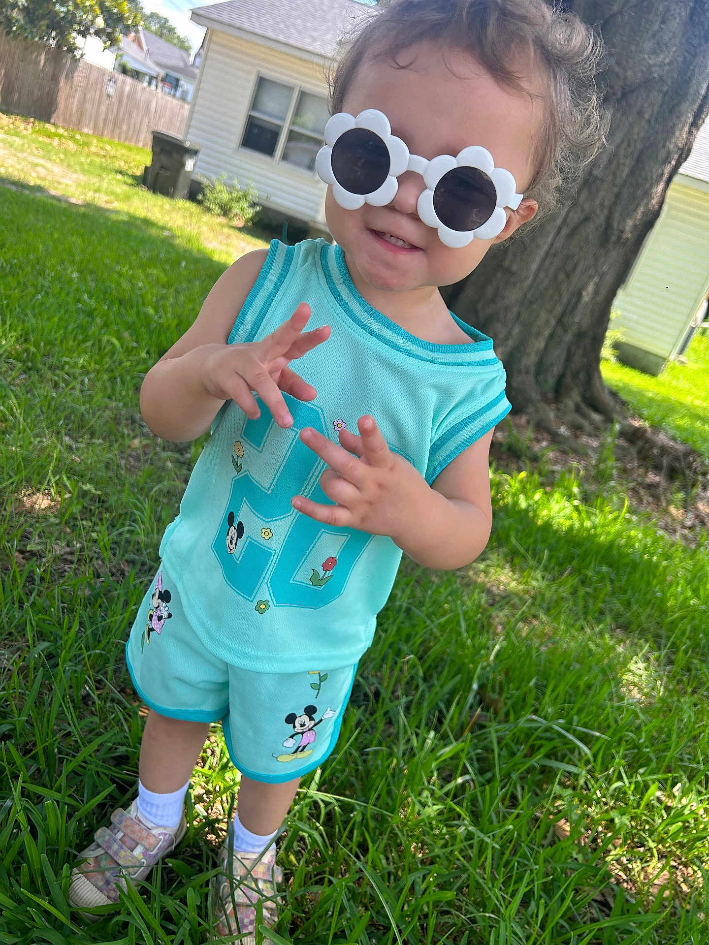 Joselyn joined the competition — help win amazing prizes! toddler, child, sunglasses, flower_shaped, turquoise_clothing, mickey_mouse, shorts, tank_top, grass, tree, house, outdoor, shoes, socks, sunny, daylight, playful, gesture, smile, person