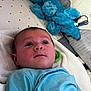 baby, infant, blue_shirt, stuffed_animal, bed, blanket, pillow, curious, lying_down, indoor, soft_toys, child, cute, young, portrait, face, person, cozy, comfort, resting