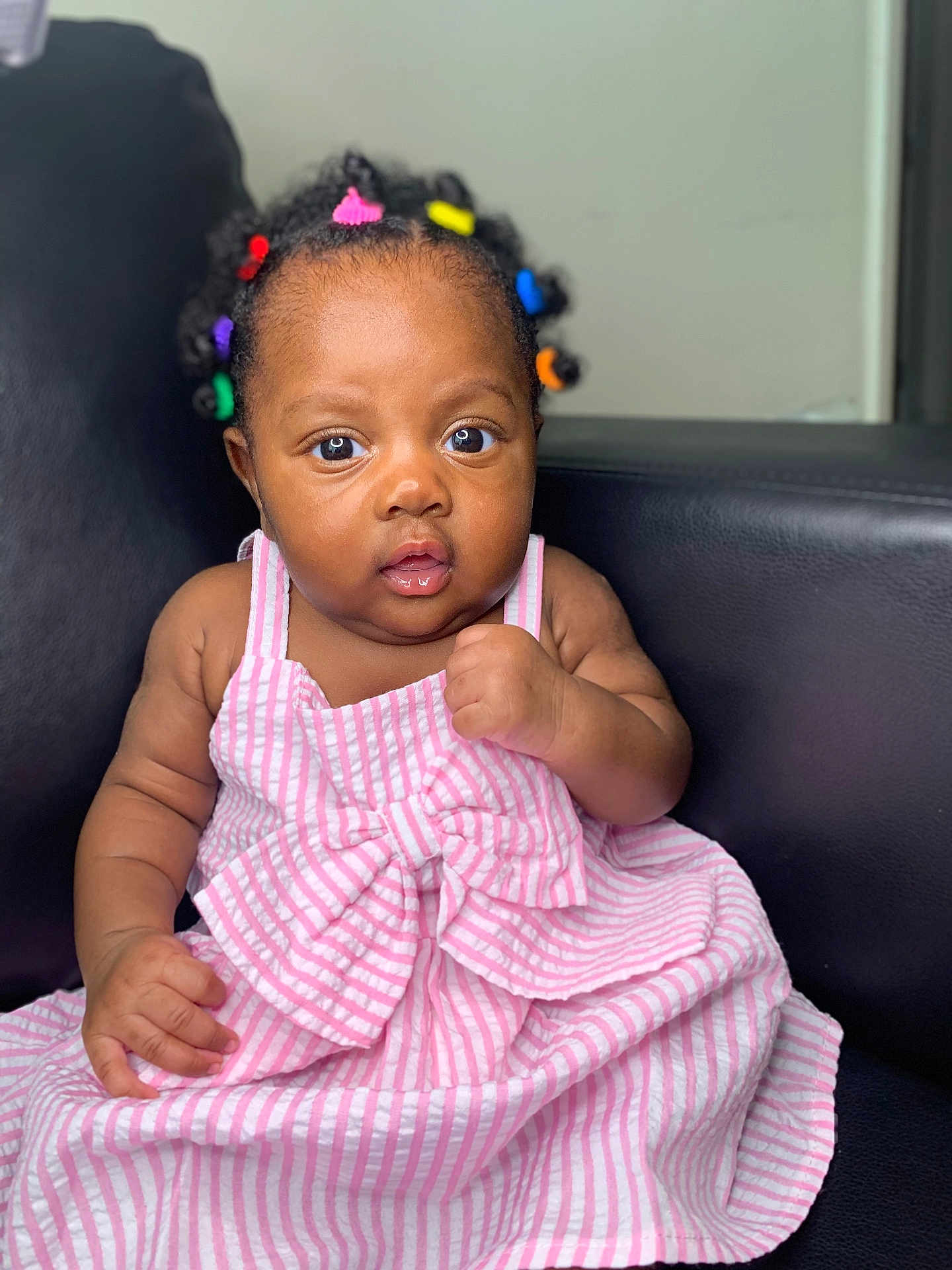 Chimamanda joined the competition — help win amazing prizes! baby, child, infant, dress, pink_stripes, bow, hair_beads, colorful, curly_hair, face, eyes, hand, sitting, chair, leather, indoor, portrait, cute, expression, skin