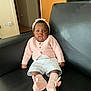 Chimamanda joined the competition — help win amazing prizes! baby, child, infant, pink_headband, pink_sweater, white_shorts, bunny_slippers, black_couch, indoor, living_room, curious_expression, sitting, furniture, home, portrait, cute, cozy, headwear, footwear, person