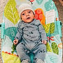 baby, infant, child, onesie, hat, bear_ears, baby_rocker, colorful, patterned, leaf_pattern, fish_pattern, carpet, floor_tiles, indoor, cute, smiling, seated, hands, feet, face