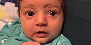 Kohen is registered to the contest to win money with this photo: baby, infant, face, hand, tattoo, clothing, blue, teal, blanket, dinosaur, cushion, portrait, curious, wide_eyes, indoor, closeup, person, expression, resting, holding