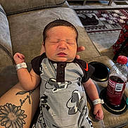 Kohen is registered to the contest to win money with this photo: newborn, baby, sleeping, infant, tattoo, arm, clothing, recliner, sofa, bottle, drink, living_room, person, hand, cute, resting, indoors, comfort, peaceful, casual