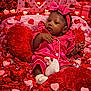 baby, infant, pink_pajamas, headband, bow, heart_shapes, red_hearts, pink_hearts, plush_pillows, love_sign, valentine_theme, beads, decorations, cute, portrait, indoor, celebration, holiday, soft_toys, relaxed