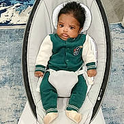 Myles is registered to the contest to win money with this photo: baby, infant, child, baby_rocker, green_clothing, white_clothing, indoor, carpet, flooring, wood_floor, face, person, sitting, modern_furniture, baby_seat, cute, young_child, expression, home_interior, comfort