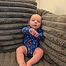 Kenneth is registered to the contest to win money with this photo: baby, infant, onesie, blue_clothing, colorful, couch, plush, cushion, soft_texture, indoor, child, person, seated, legs, feet, head, face, relaxed, expression, cozy