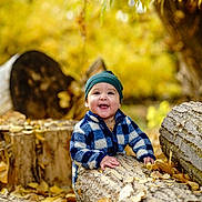Rodrigo is registered to the contest to win money with this photo: baby, child, smiling, outdoor, autumn, leaves, logs, nature, fall, tree, wood, happy, person, cute, jacket, beanie, seasonal, forest, playful, portrait