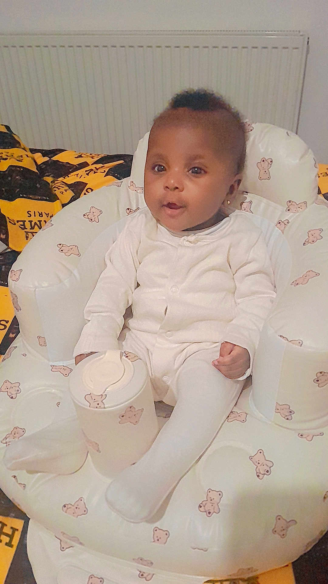 Elizabeth is registered to the contest to win money with this photo: baby, child, infant, white_clothing, baby_chair, teddy_bear_pattern, container, indoor, blanket, cushion, cute, portrait, seated, young_child, comfort, home, furniture, person, soft, adorable