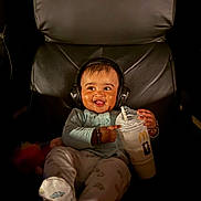 Rugvednandan is registered to the contest to win money with this photo: baby, beverage, candid, chair, clothing, cute, dark_background, drink, expression, footwear, happy, headphones, indoor, infant, mcdonalds, person, portrait, relaxing, seat, smile