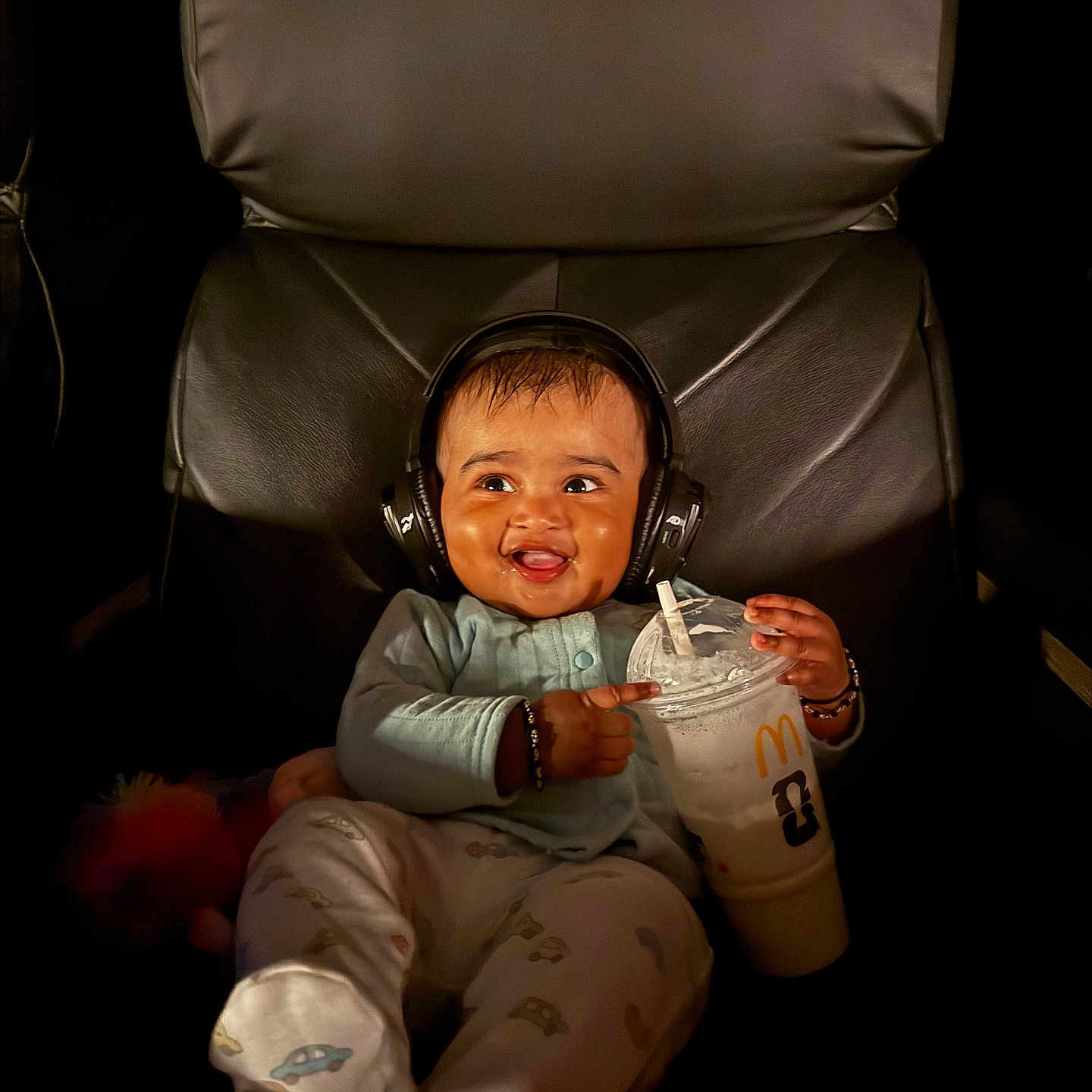 Rugvednandan is registered to the contest to win money with this photo: baby, beverage, candid, chair, clothing, cute, dark_background, drink, expression, footwear, happy, headphones, indoor, infant, mcdonalds, person, portrait, relaxing, seat, smile