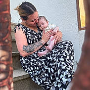Maylann participe au concours pour gagner de l'argent avec cette photo : affection, baby, baby_clothes, casual_clothing, closeup, emotion, face, holding, love, natural_light, outdoor, patterned_dress, person, portrait, sitting, skin, staircase, stairs, tattoo, woman
