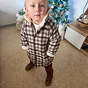 Sawyer participe au concours pour gagner de l'argent avec cette photo : brown_shoes, cabinet, checkered, child, christmas_tree, coat, curious, curly_hair, festive, floor, furniture, holiday_decorations, indoor, lights, ornaments, portrait, standing, toddler, toy, winter_clothing