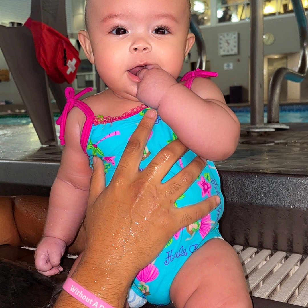 Laylani Dailynn joined the competition — help win amazing prizes! adult_hand, baby, chair, child, clock, colorful_clothing, curious, face, hand, indoor, infant, person, playful, pool, skin, support, swimsuit, water, water_splash, wet