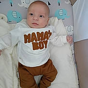 Liam a rejoint le concours — aidez-le/la à gagner de superbes lots ! baby, infant, crib, mattress, elephant_pattern, white_shirt, brown_pants, black_socks, lying_down, child, indoors, blanket, cute, young_child, resting, person, infant_clothing, face, head, calm